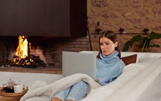 Femme sur un ordinateur dans un fauteuil, à côté d'un feu ouvert