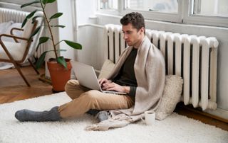 Homme assis par terre avec un ordinateur, adossé à un radiateur