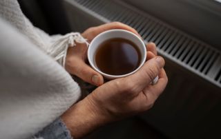 Mains tenant une tasse de café au-dessus d'un radiateur